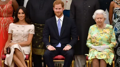 Reuters Britain's Queen Elizabeth, Prince Harry and Meghan, the Duchess of Sussex sit in a line against a backdrop of some of Queen"s Young Leaders at a Buckingham Palace reception following the final Queen"s Young Leaders Awards Ceremony, in London, Britain June 26, 2018.