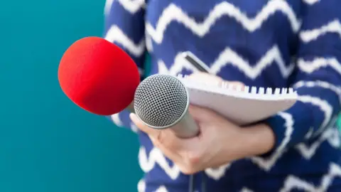 Getty/Mihajlo Maricic / EyeEm Midsection Of Journalist Holding Microphone And Book - stock photo