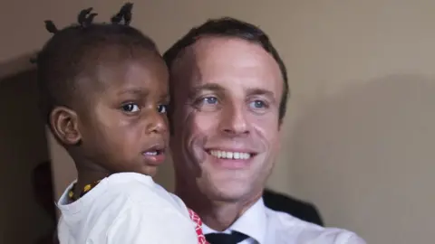 Getty Images French President Emmanuel Macron holds a child as he meets residents of Quartier Orleans, 29 September 2018