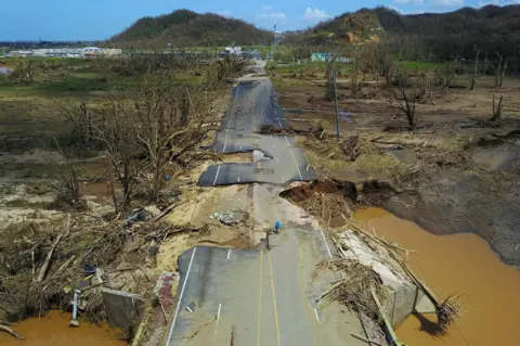 RICARDO ARDUENGO/ EPA A man cycles on a destroyed road in Toa Alta, Puerto Rico.