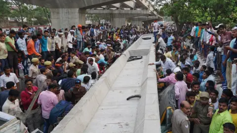 AFP Indian bystanders gather at the site of a flyover collapse in Varanasi on May 15, 2018. At least sixteen people have been killed after a flyover collapsed on a street in Varanasi, the Press Trust of India reported.