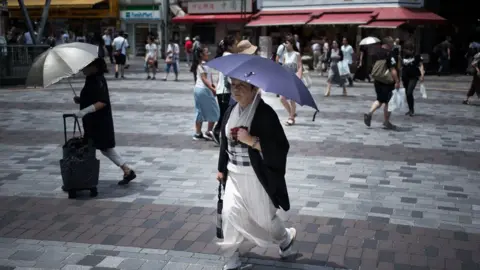 Getty Images A woman holds an umbrella as she walks along a street in Tokyo on July 23, 2018, as Japan suffers from a heatwave