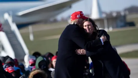 AFP via Getty Images Donald Trump hugs his former press secretary Sarah Huckabee Sanders during a Make America Great Again rally at Dubuque Regional Airport