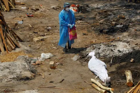 Adnan Abidi / Reuters A woman wearing PPE stands next to the body of a family member in New Delhi, India