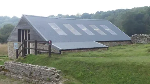 B Russell A stone building with a modern, wooden, grey roof and skylight windows.