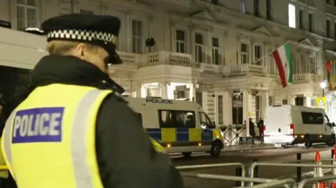 A police officer in a hi vis jacket is seen stood outside the Iranian embassy 