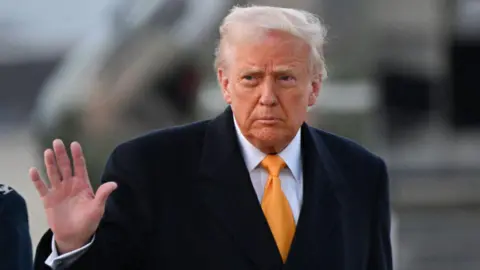 Getty Images US President Donald Trump in a black overcoat and suit waves to reporters as he walks outside