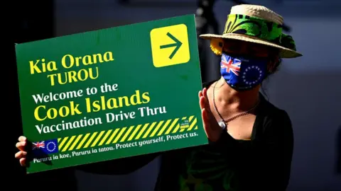 Getty Images A woman holds a sign for a Cook Islands vaccination drive through, September 2021