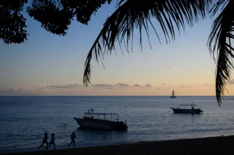 Philippe Lopez/AFP Children run on a beach while a boat sails off the coast of French territory Mayotte, near Kani Keli - Saturday 27 May 2023