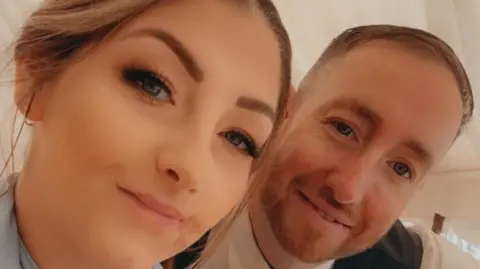 Laura and her partner are posing together in a close-up image. She has her hair tied back and he has short brown hair and a short beard.