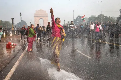 Getty Images A protester chants slogans as she braces herself against the spray fired from police water canons during a protest against the Indian government's reaction to recent rape incidents in India, in front of India Gate on December 23, 2012 in New Delhi, India.