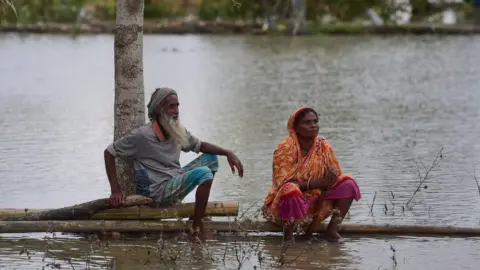 Getty Images A marooned couple sit on a log close to their home, surrounded by flood water following the cyclone on May 4