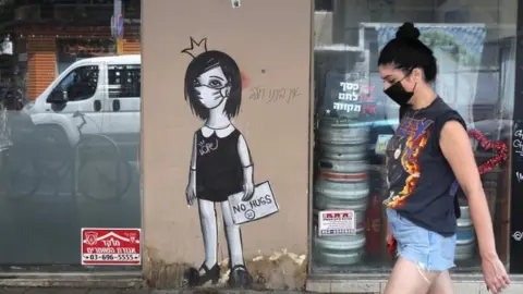 EPA A woman walks by coronavirus graffiti in Tel Aviv (8 September 2020)