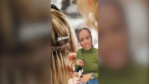 Woman in green top holding small microphone in front of green screen image of a woman's hair