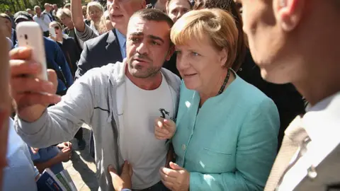 Getty Images German Chancellor Angela Merkel pauses for a selfie with a migrant