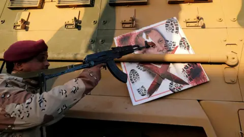 Reuters A solider loyal to Gen Hafter points his gun at the image of Turkish President Tayyip Erdogan stuck to an armoured vehicle in Benghazi - January 2020