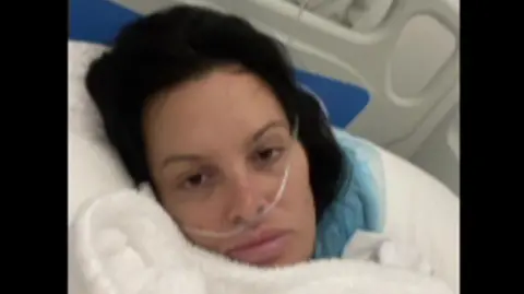 Handout A woman with dark hair lying in a hospital bed. She has a breathing tube inserted into her nose.
