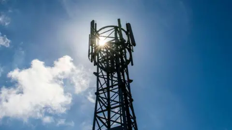 We can see the top of a mobile phone mast tower. The sun shines through the top of it.