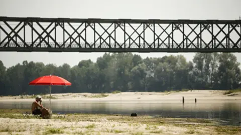 AFP A young man sits under an umbrella at the Po River near the Ponte della Becca bridge in Linarolo, near Pavia, northern Italy