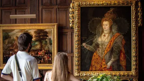 Hatfield Park Two people, with their backs to the camera, looking at The Rainbow Portrait, a painting of Queen Elizabeth I at Hatfield House, with another painting next to it