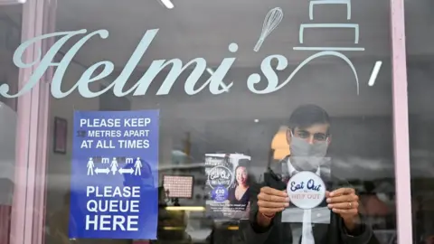 PA Media Chancellor of the Exchequer Rishi Sunak places an Eat Out to Help Out sticker in the window of a business during a visit to Rothesay on the Isle of Bute, Scotland.