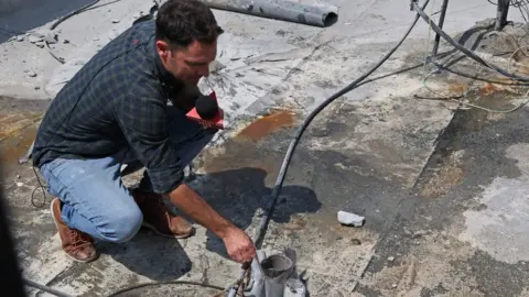 Getty Images A reporter holds the remains of a rocket launched from the Gaza Strip, in the southern Israeli city of Sderot on August 6, 2022. -