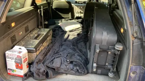 Car boot with suitcase and various sheets and boxes.