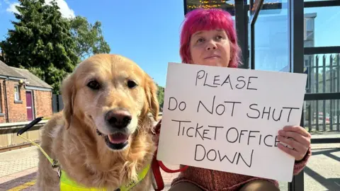 Sarah Leadbetter Sarah Leadbetter holding a 'Please do not shut ticket offices down' sign alongside her guide dog, Nellie