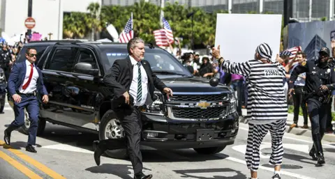 EPA A protester runs out in front of former President Donald Trump's motorcade as it departs the Wilkie D. Ferguson United States Courthouse