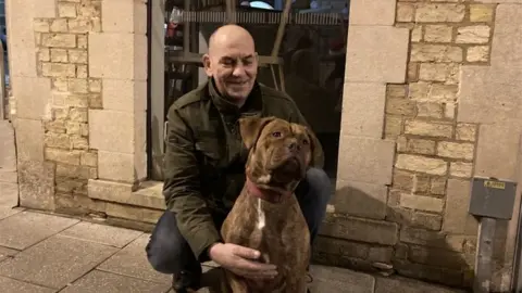 Vinny crouches down behind dog Cali.