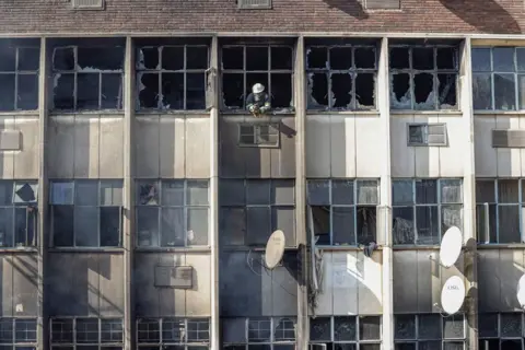 Michele Spatari / AFP A firefighter looks out of broken windows at the scene of a fire in a building in Johannesburg
