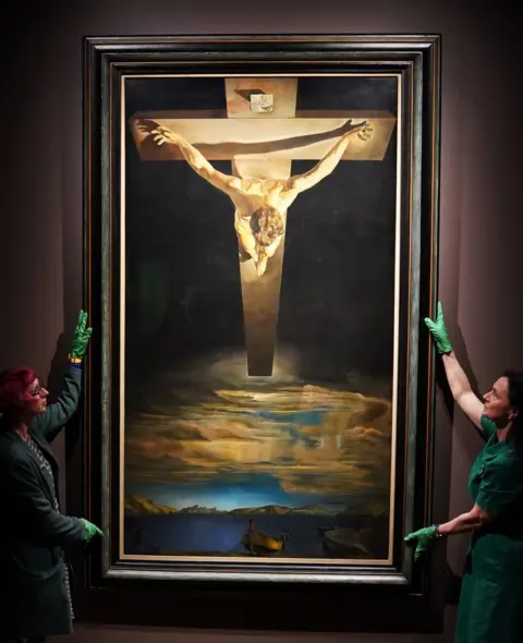 PA Media Dr Jo Meacock (left), curator from Glasgow Art Museum and Morlin Ellis, curator at the Spanish Gallery in Bishop Auckland during the installation of Salvador Dali's painting Christ of St John of the Cross at the Spanish Gallery in Bishop Auckland, County Durham.