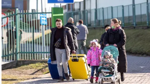 Getty Images A family with a toddler and a child in a pram, trailing suitcases, cross into Poland