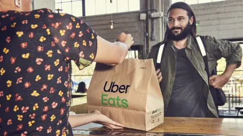 Uber An Uber Eats driver picks food up at a restaurant.