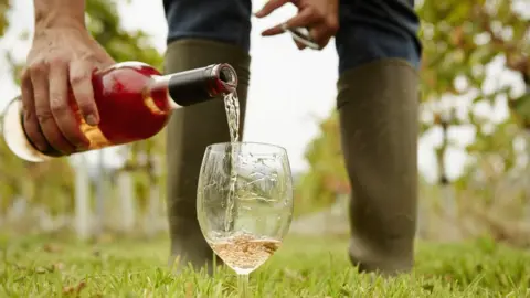 Getty Images A man in wellies pouring a glass of wine