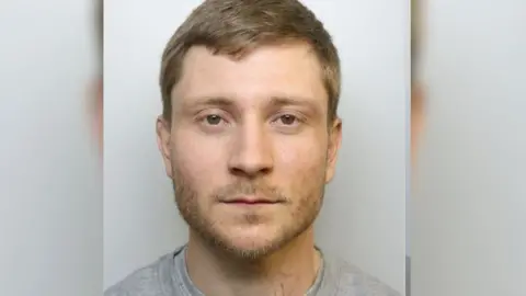Mugshot of Jones who is wearing a grey top and has brown hair and beard