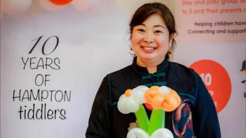 Faustina Yang smiling while standing in front of a '10 years of Hampton Tiddlers' board