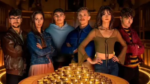 Final contestant of the show Jack, Rachel, Faraaz, Stephen, Jade and James stand around a table laden with gold.