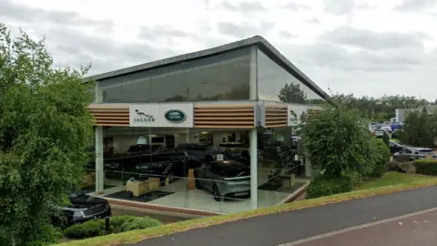 A street view of the Land Rover and Jaguar garage which is a glass building. Cars can be seen inside the building.