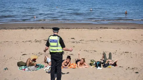 Getty Images Policeman talks to sunbathers on beach