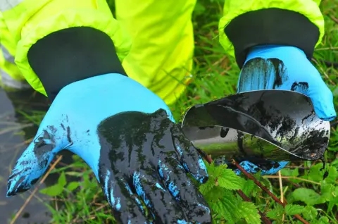 Environment Agency 'Black sludge' on blue gloves