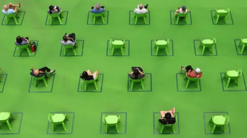 Getty Images People sit on chairs marked out to maintain social distancing amid the COVID-19 pandemic on 19 March 2021 in Singapore