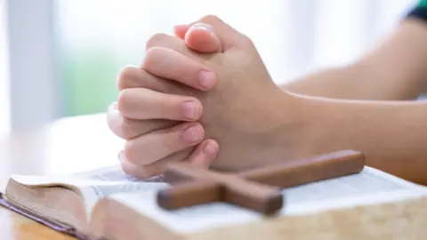 GETTY IMAGES A child prays. there's a wooden cross lying on top of a bible.