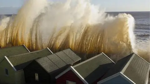 Alamy Large wave crashing to the shore in front of houses