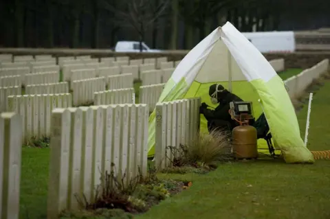 CWGC Person covered by a small tent repairing a headstone at Delville Wood Cemetery in France