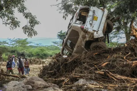 DANIEL IRUNGU/EPA People look at a damaged car after flash floods in Mai Mahiu, in the Rift Valley region of Naivasha, Kenya, on 30 April.