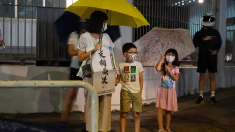 Getty Images A woman holds a copy of the Apple Daily newspaper in front of the Apple Daily headquarters with her children