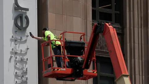 Reuters A worker uses a smartphone while dismantling a Twitter's sign at Twitter's corporate headquarters building as Elon Musk renamed Twitter as X and unveiled a new logo, in downtown San Francisco