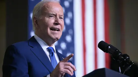 Joe Biden speaks in Wisconsin on 8 May wearing a blue tie with a US flag in the background