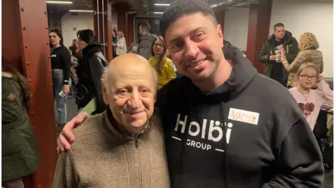 Yeugen and Vadym Gurevych, father and son at "The Table" standing together. Vadymn has his arm around his father